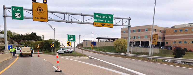 Photo of curve on State Route 54 with high-friction surface treatment applied on the pavement in the right lane and work truck parked in the left lane.